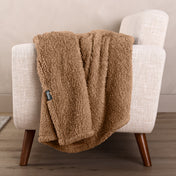 Faux shearling blanket draped over a beige armchair with a wooden base.