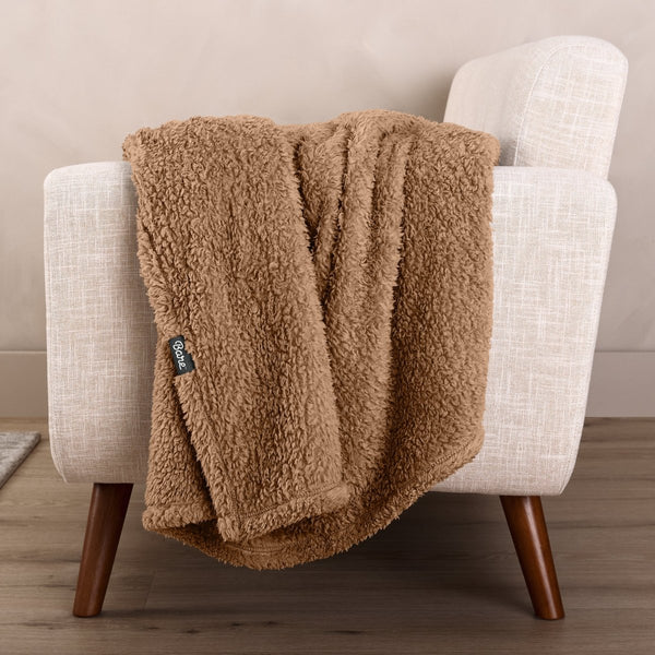 Faux shearling blanket draped over a beige armchair with a wooden base.