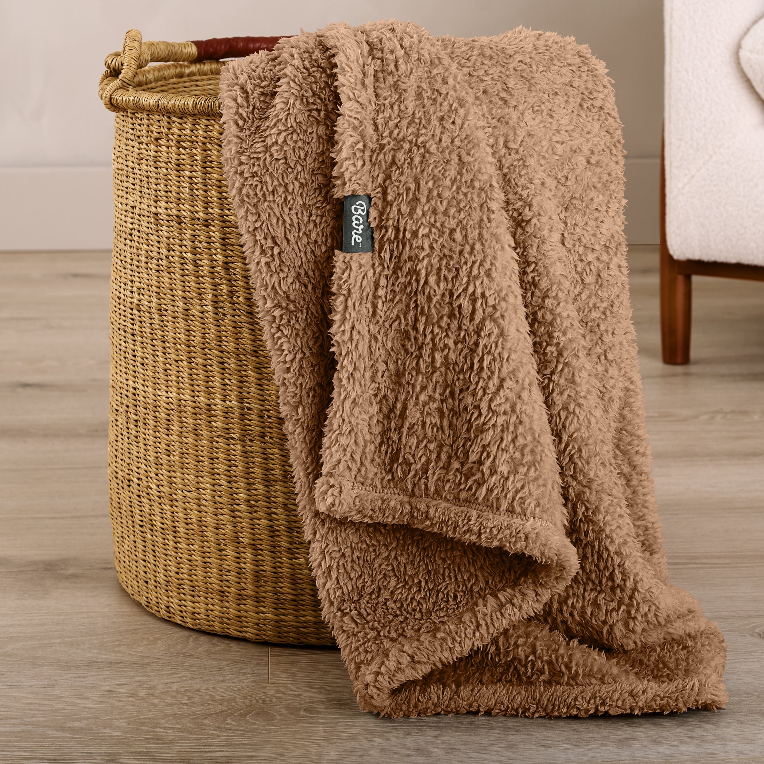 Fluffy blanket draped over a woven basket on a wooden floor.