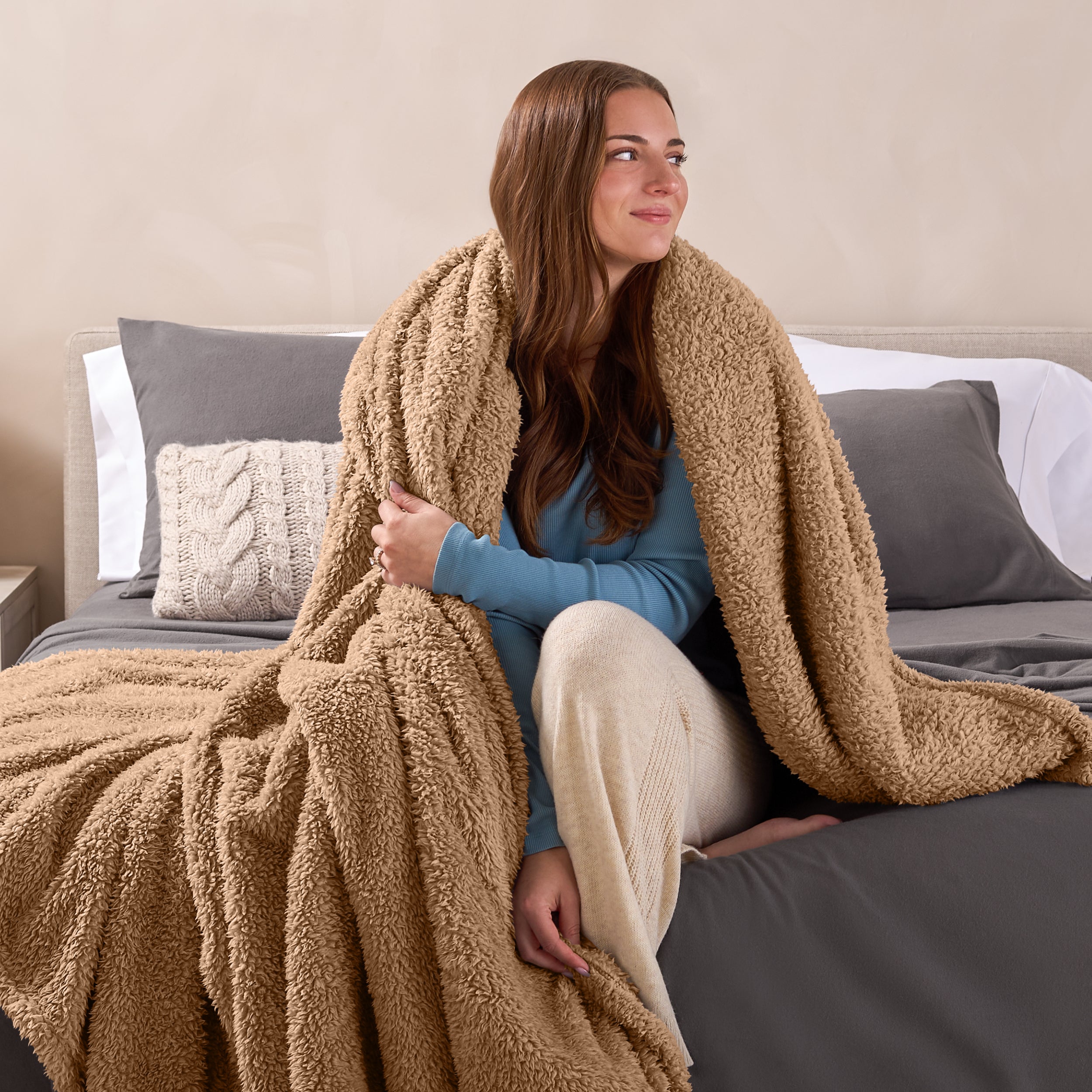 A woman sitting on a bed wrapped in a sherpa blanket