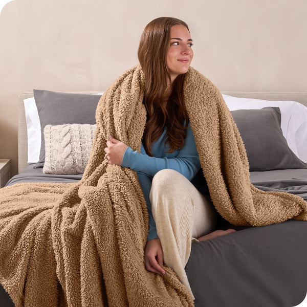 A woman sitting on a bed wrapped in a sherpa blanket