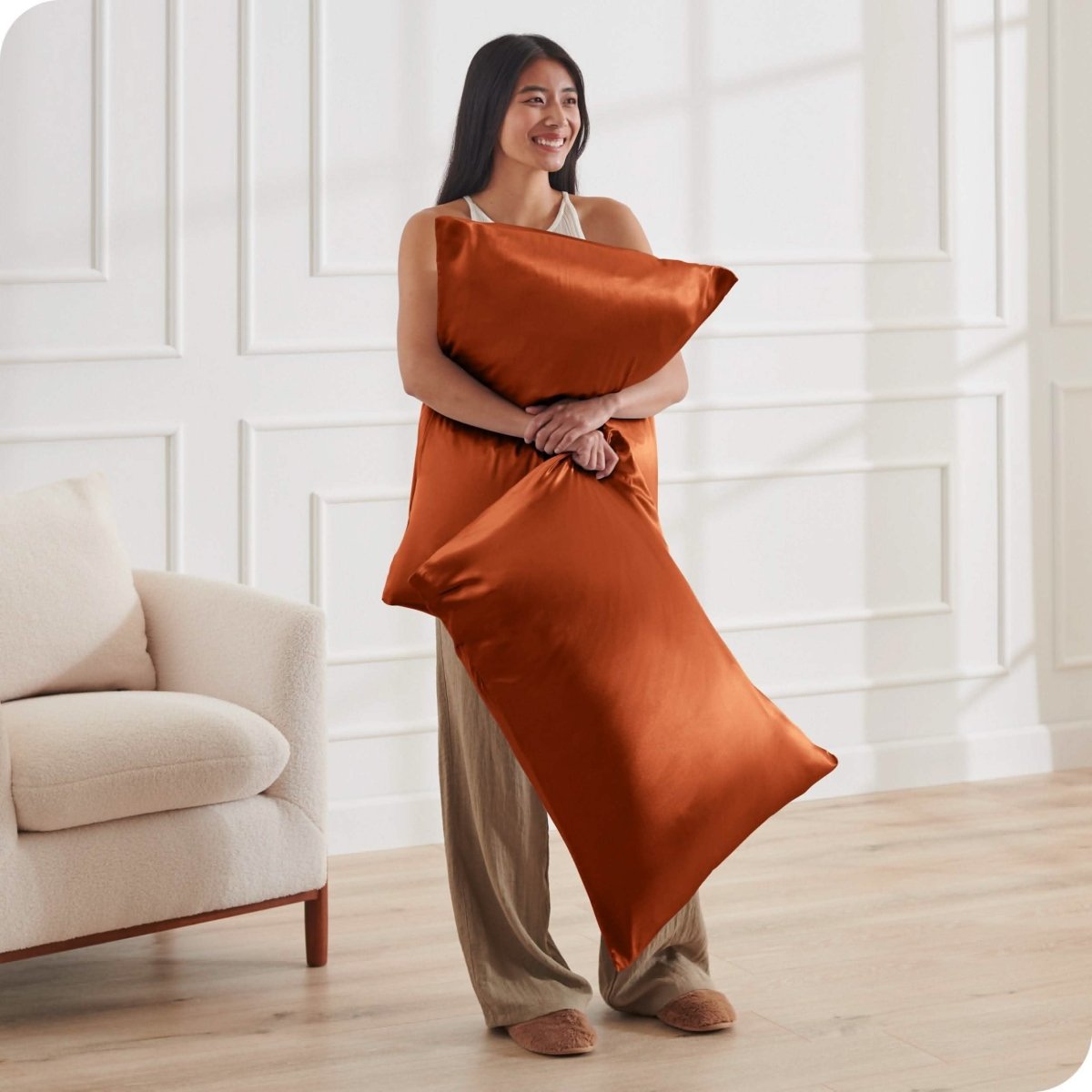 A woman standing while holding pillows with silk pillowcases on them