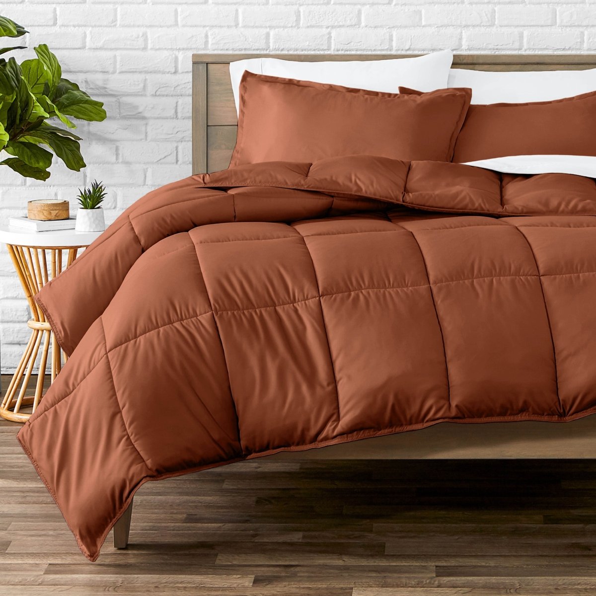 Comforter set on a bed with a white brick wall and plant in the background