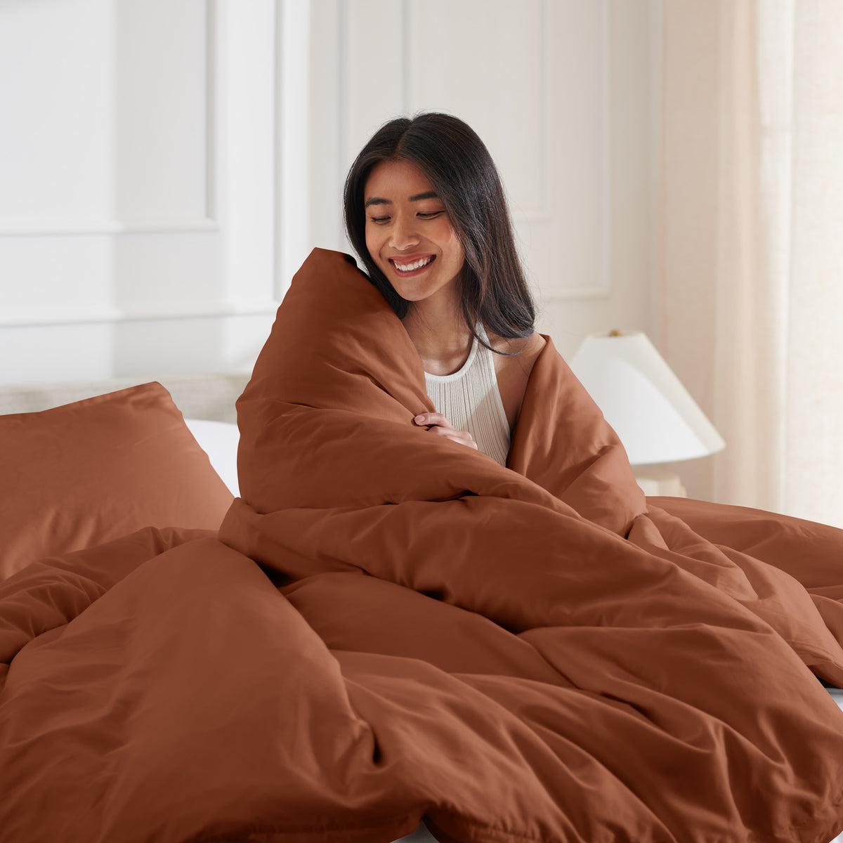 Woman smiling under duvet cover set in a bedroom setting