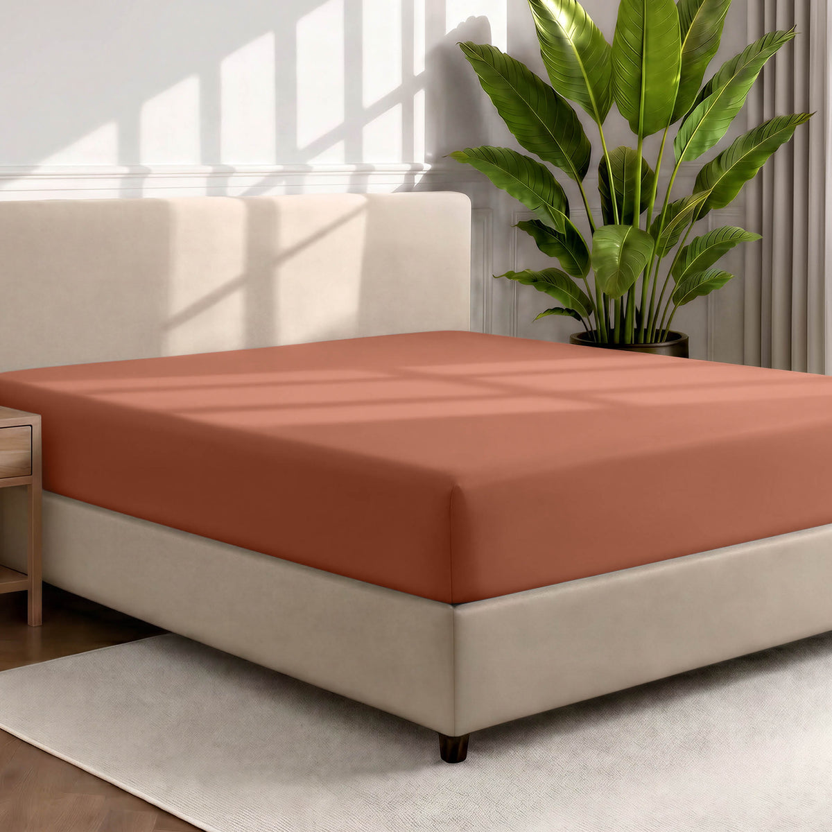 Bed with a fitted sheet in a room with a large plant and rug