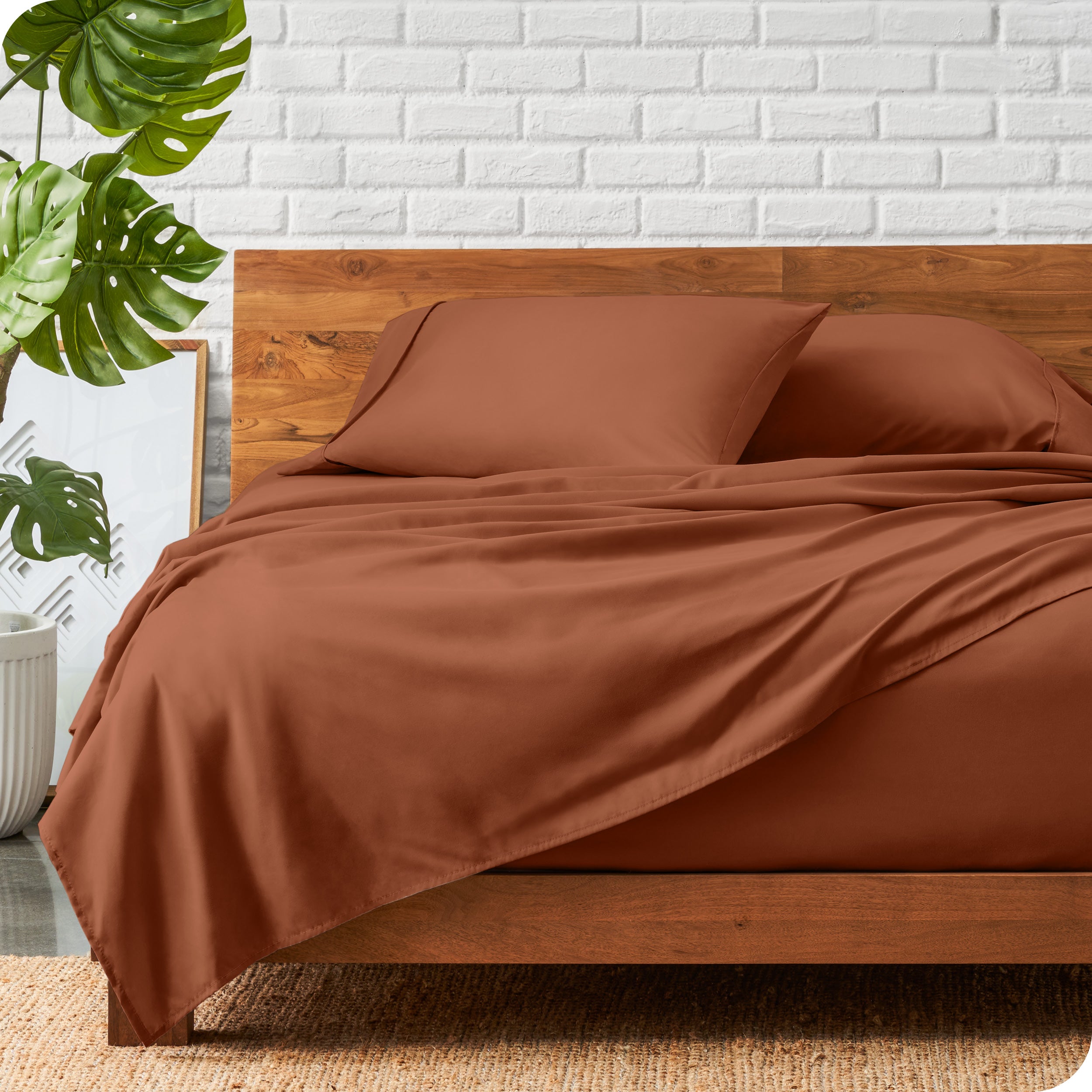 A wooden bed frame with a microfiber sheet set on the mattress.