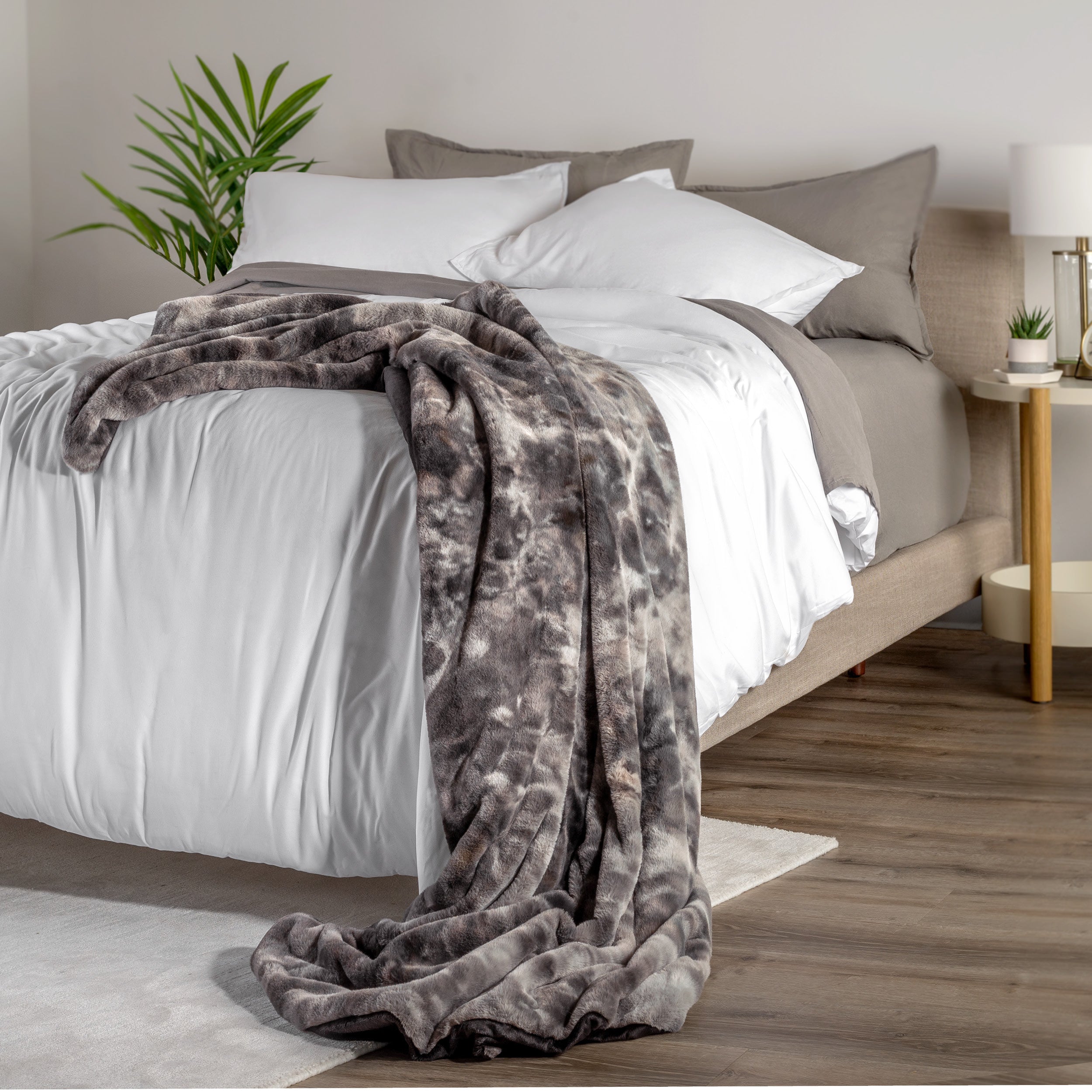 Blanket draped over a bed in a bedroom setting with a nightstand and lamp.