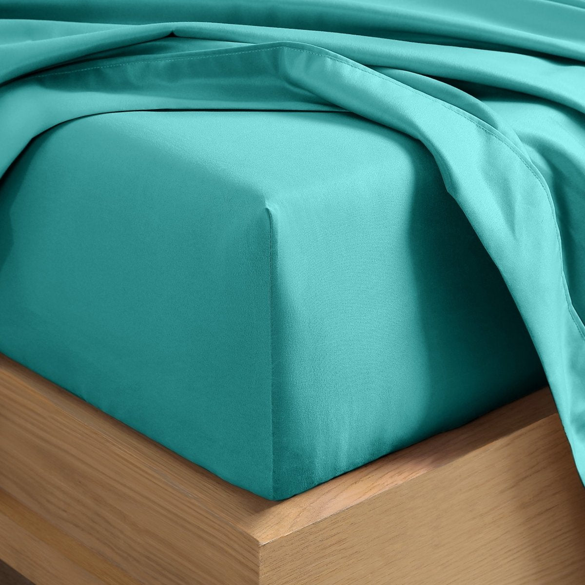 A close-up of a fitted sheet covering the corner of a bed frame, with matching top sheet draped over it.