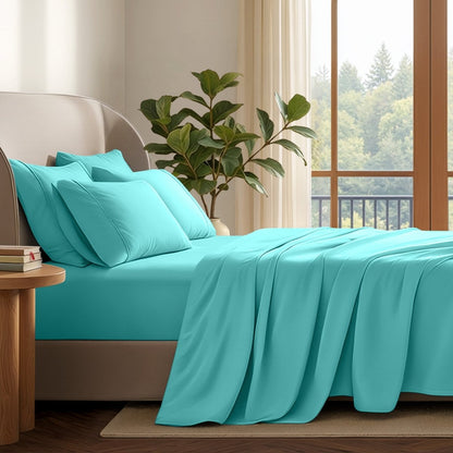 A neatly made bed with in a softly lit bedroom. A large green plant stands beside the bed, and a window with curtains is visible in the background.