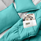 Comforter and pillows on a bed with a magazine and glasses.