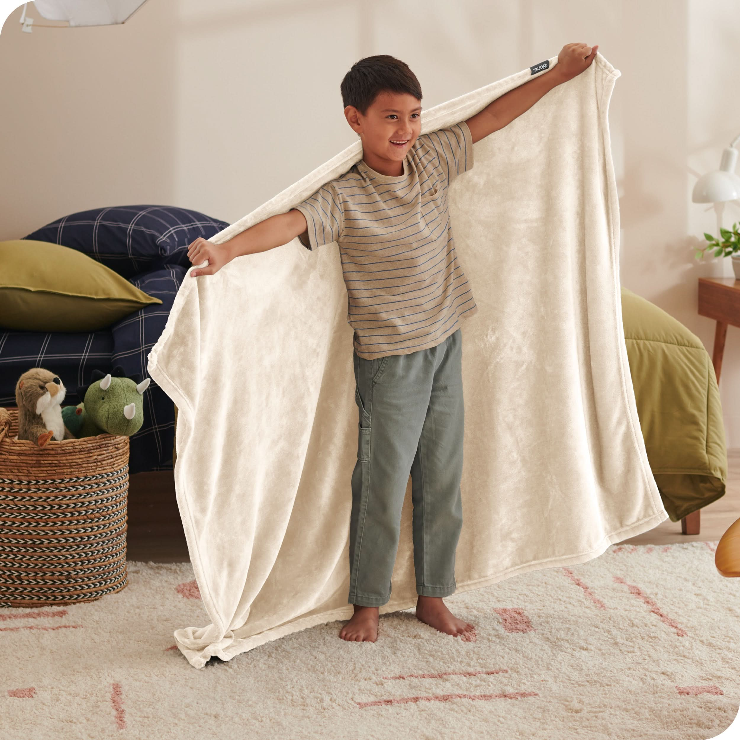 A child has his arms stretched out while holding a microplush blanket behind him