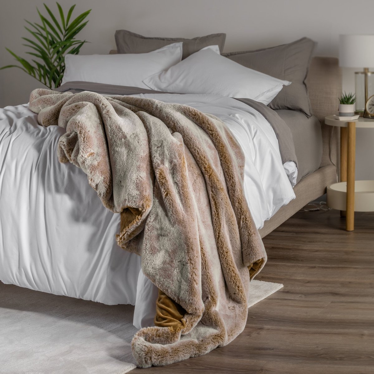 Blanket draped over a bed in a bedroom setting with a nightstand and lamp.