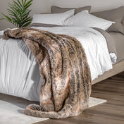 Blanket draped over a bed in a bedroom setting with a nightstand and lamp.