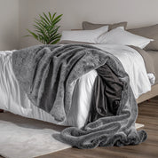 Blanket draped over a bed in a bedroom setting with a nightstand and lamp.