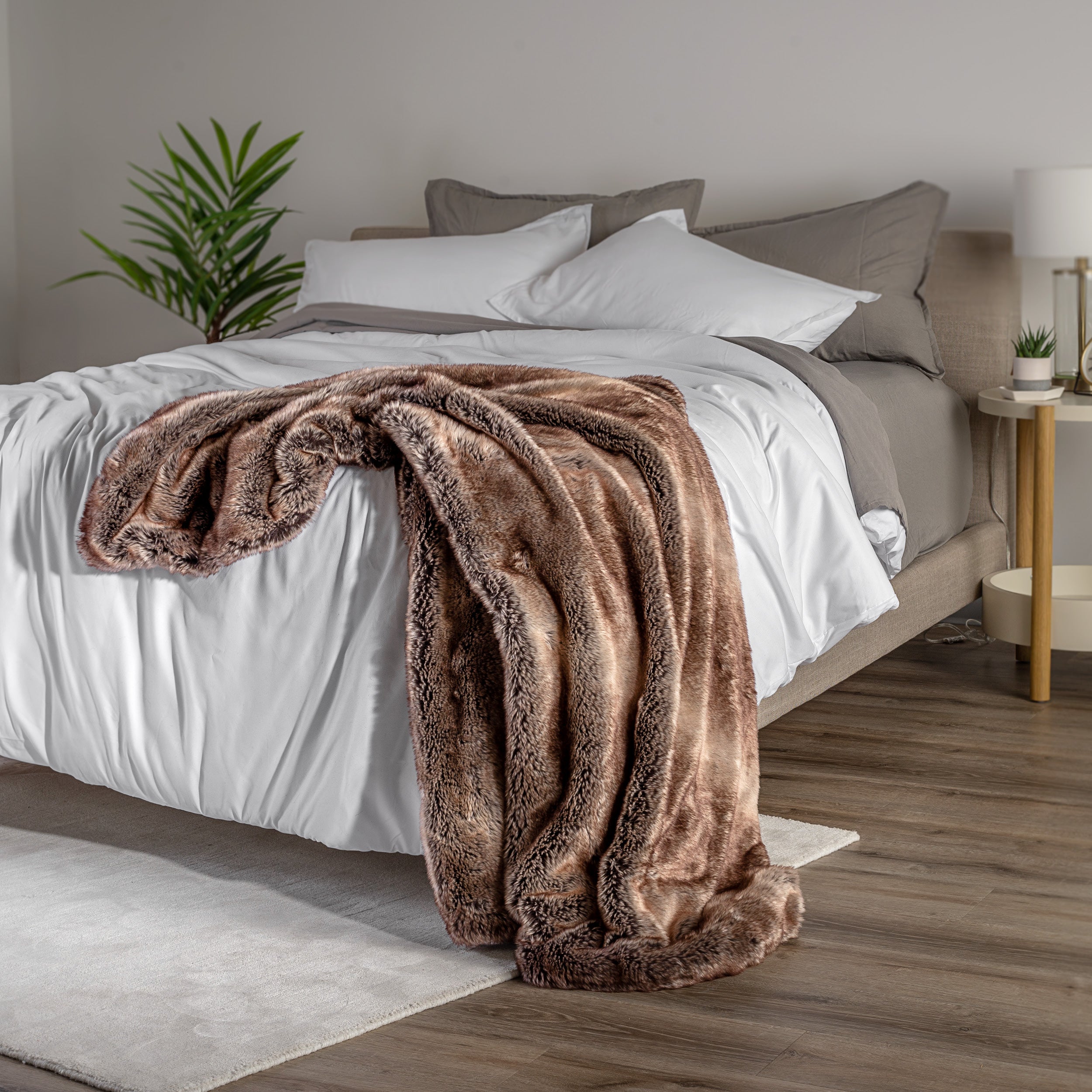 Blanket draped over a bed in a bedroom setting with a nightstand and lamp.