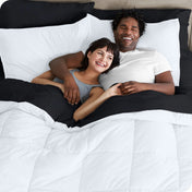 A couple is lying in bed with a comforter and sheets over them