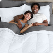 A couple is lying in bed with a comforter and sheets over them