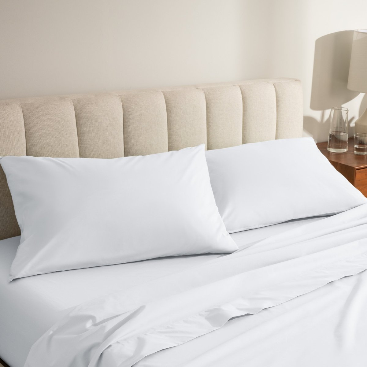 Percale bed sheets and pillowcases on a neatly made bed with a beige headboard.