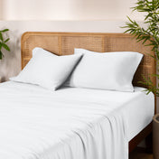 Bamboo bed sheets and pillows on a bed with a wicker headboard and plants in the background.