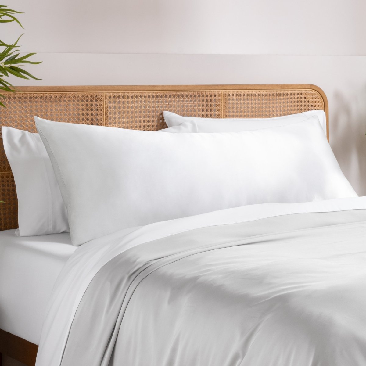 Body pillowcase on a pillow set on a bed with a wicker headboard and a plant in the corner.