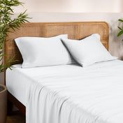 Bamboo bed sheets and pillows on a bed with a wicker headboard in a room with plants.