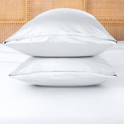 Two white pillows stacked on a bed with a woven headboard.