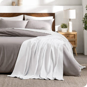A cotton waffle blanket is on the corner of a bed. It is hanging down the side and end of the bed.