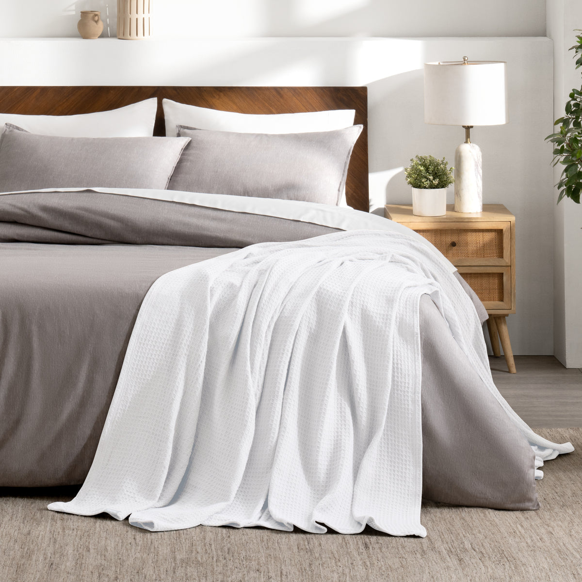 Bed with gray bedding and a throw blanket in a bedroom setting.