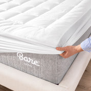 A corner of a mattress on a wood frame. A mattress pad is covering the mattress.