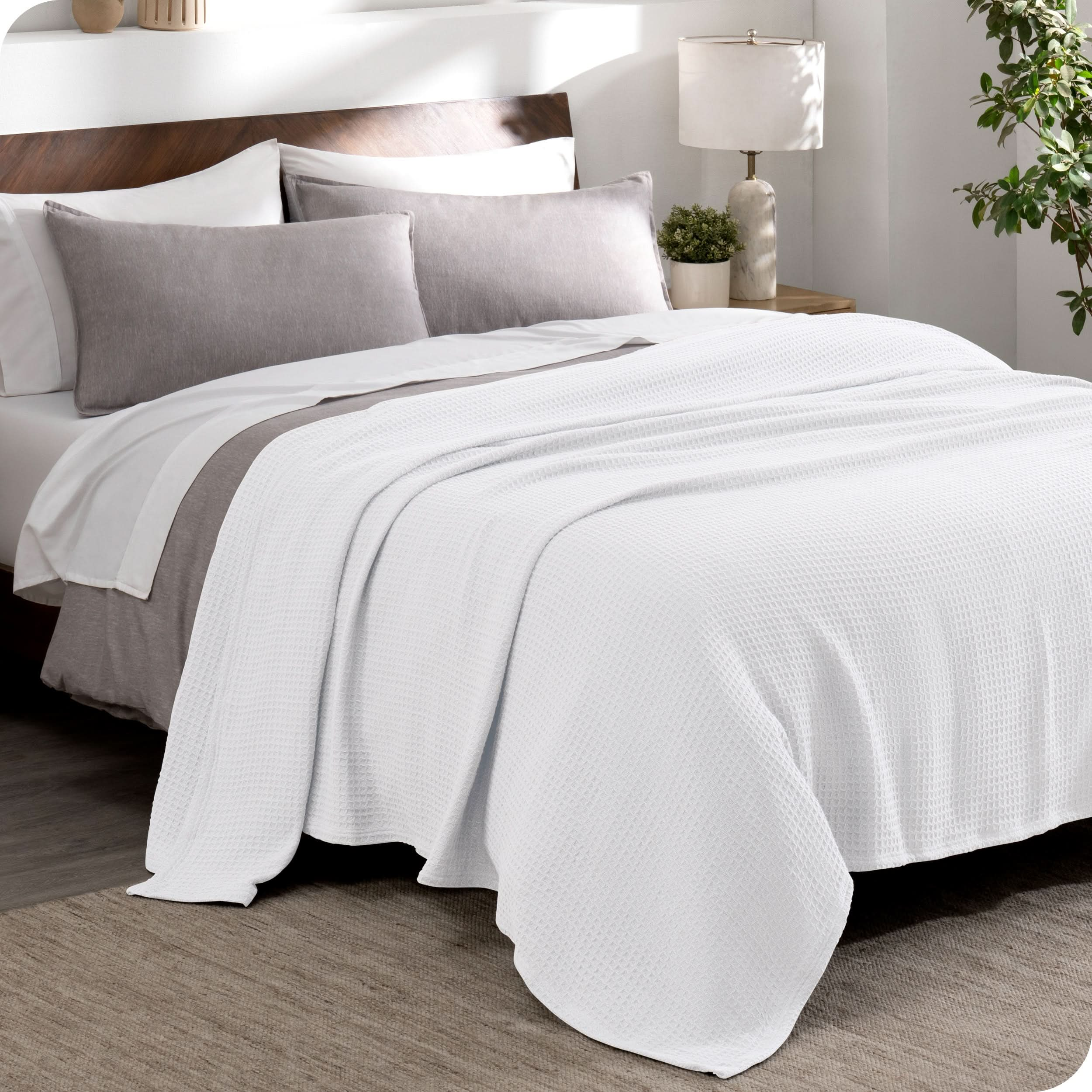 A cotton waffle blanket draped over the top of a bed made with a duvet set