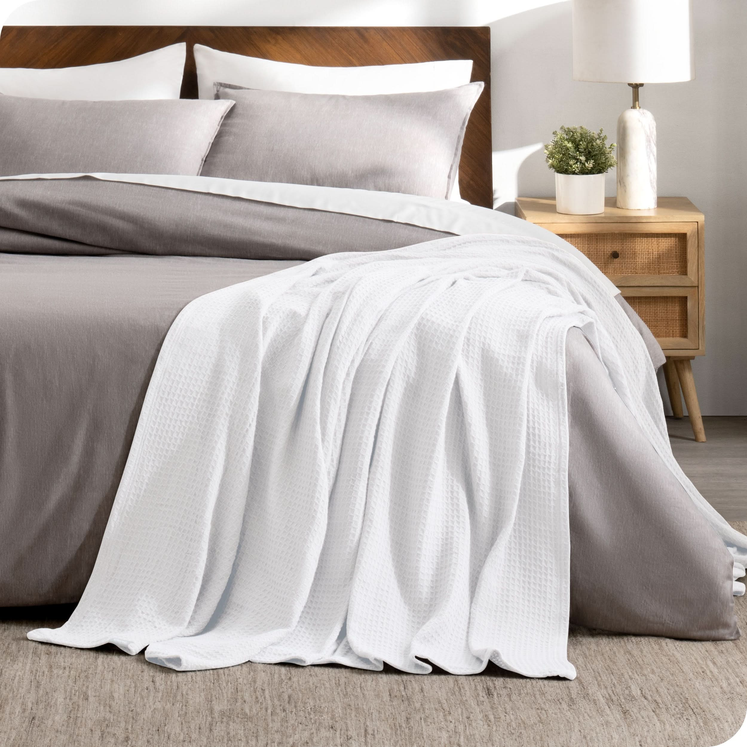 A cotton waffle blanket is on the corner of a bed. It is hanging down the side and end of the bed.