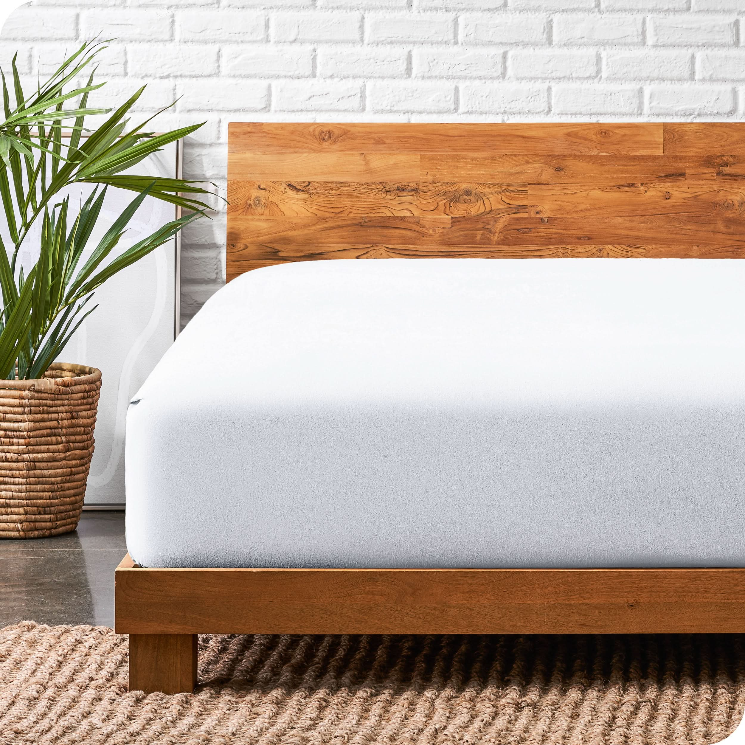 A modern bed with a wooden bed frame with a flannel fitted sheet on.