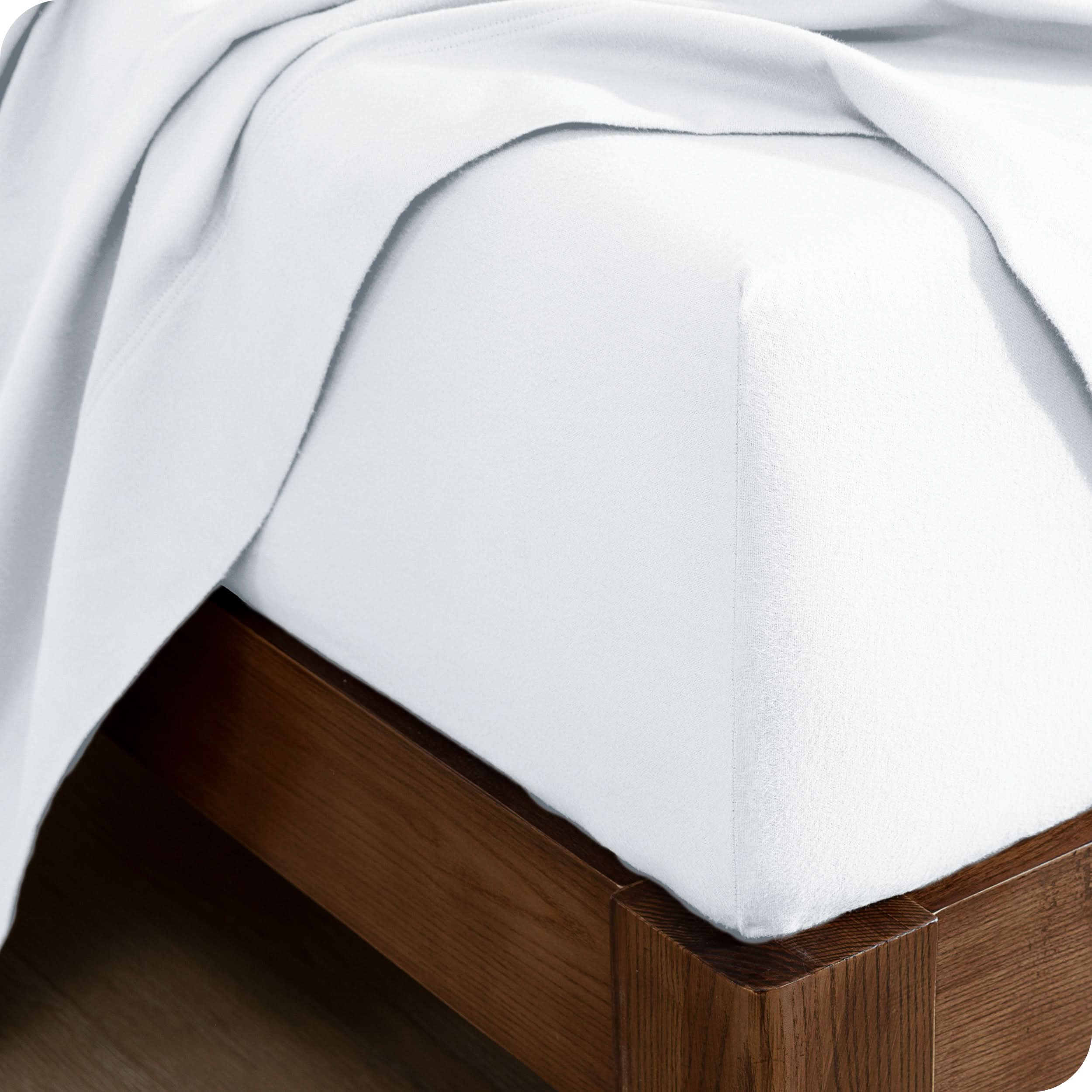 A close up of a corner of a modern bed with a flannel fitted sheet on.