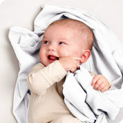 A baby lying on a receiving blanket. She has her thumb in her mouth.