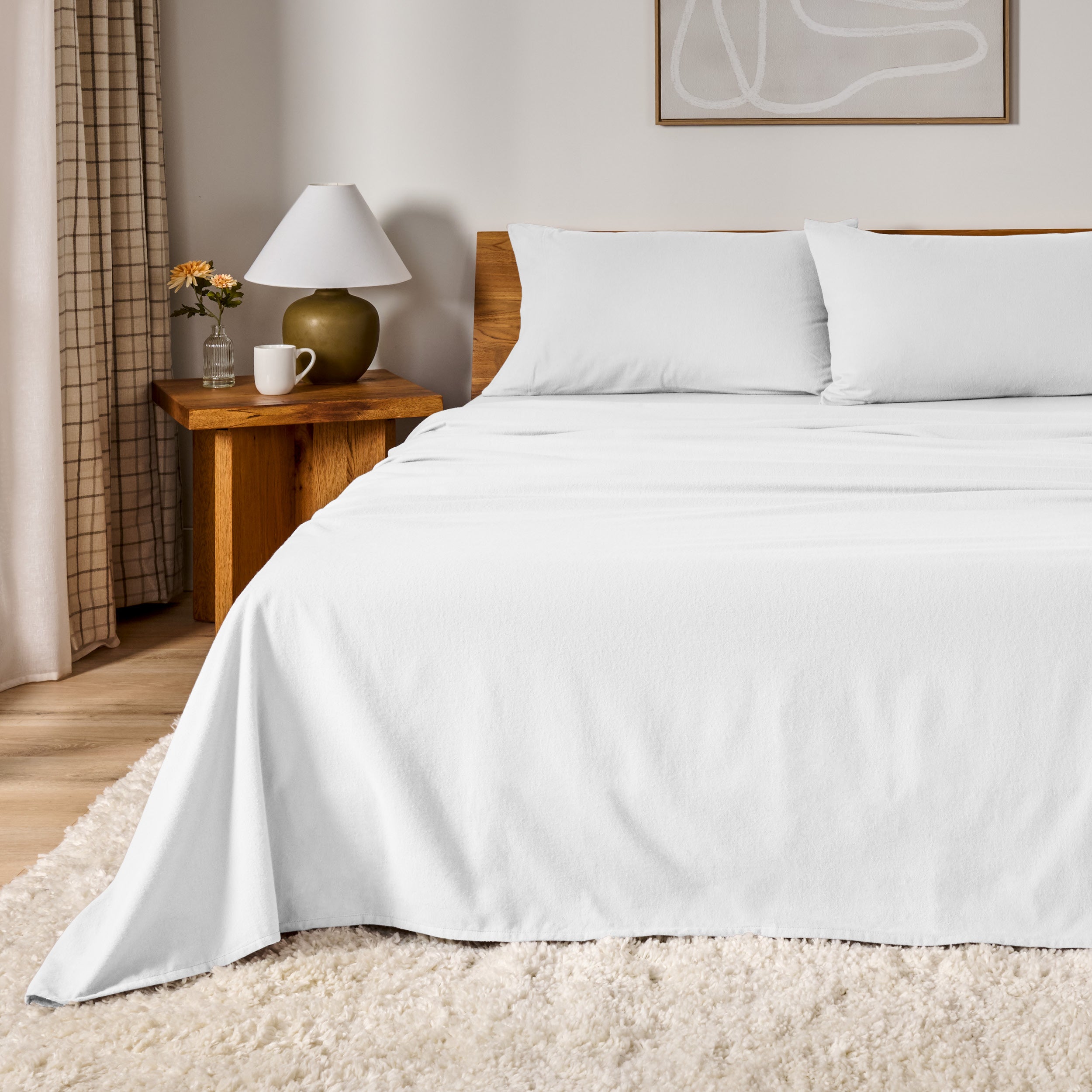 A bed dressed in flannel sheet set in a bedroom with a wooden headboard, bedside table and lamp
