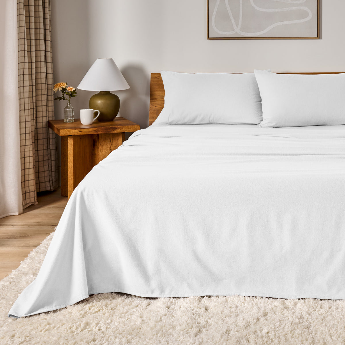 A bed dressed in flannel sheet set in a bedroom with a wooden headboard, bedside table and lamp