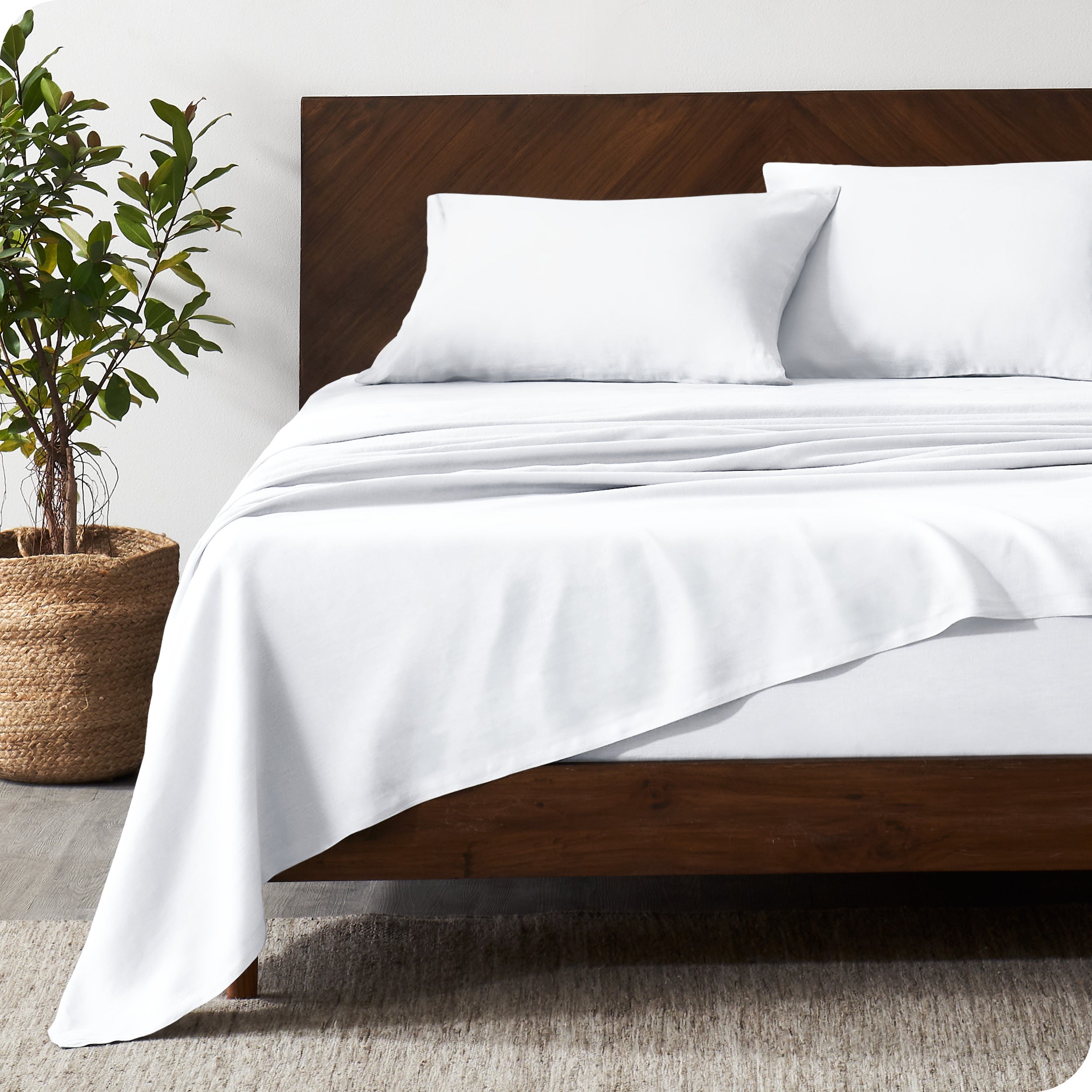 Dark wooden bed frame with white linen sheets on the mattress
