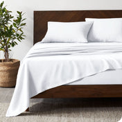 Dark wooden bed frame with white linen sheets on the mattress