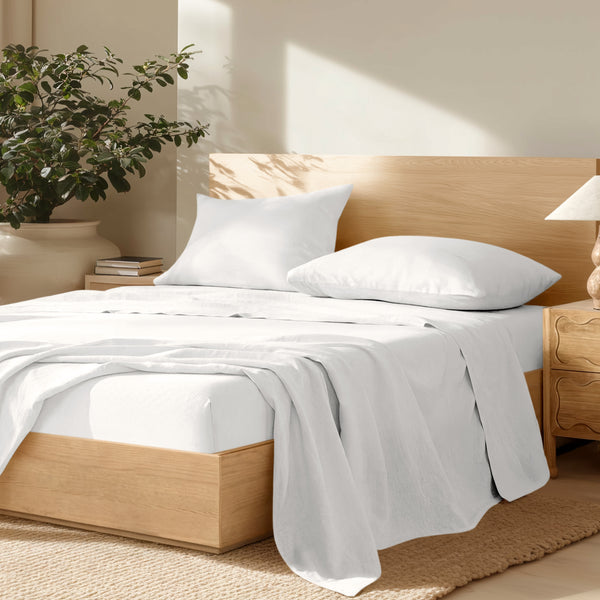 Bedroom with wooden bed frame, linen bedding, and a plant on a nightstand.