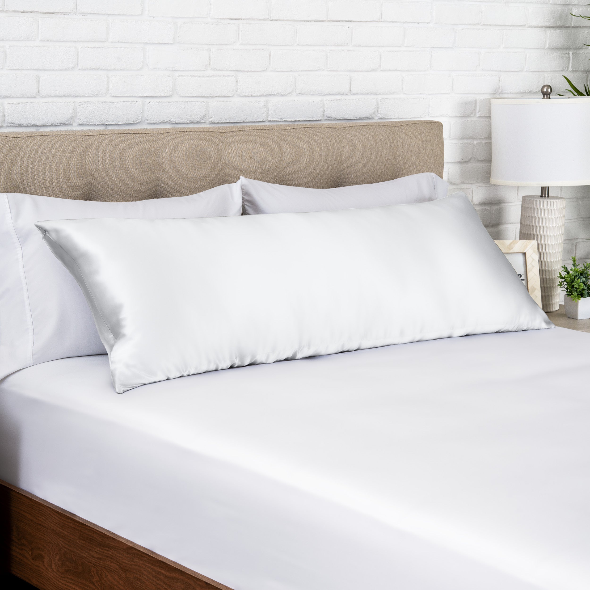 White silk pillow on a bed with white bedding and a beige headboard.