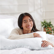 Woman lying on a bed with a body pillow, smiling.