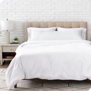 Bed with white bedding and satin pillowcase against a white brick wall.