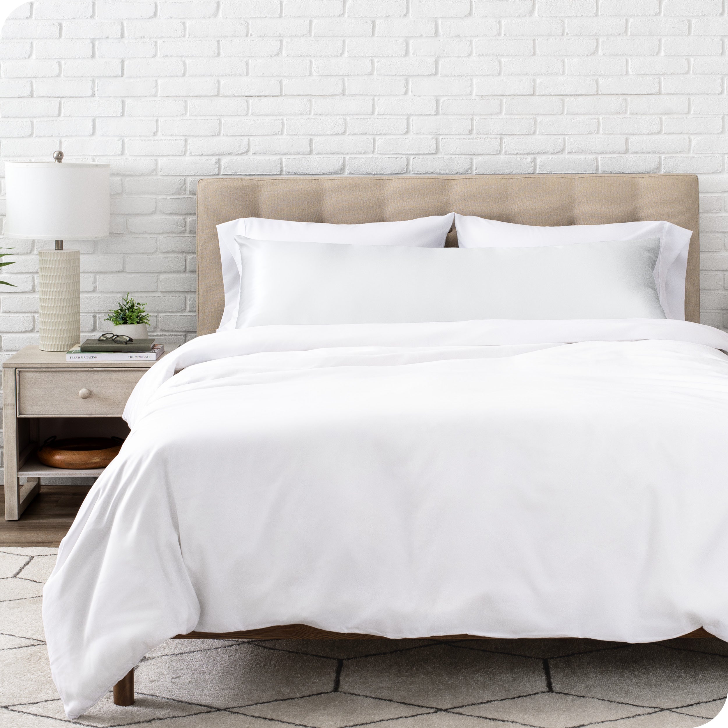 White bedding set with body pillow covered with a silk pillowcase on a bed in a bedroom setting.