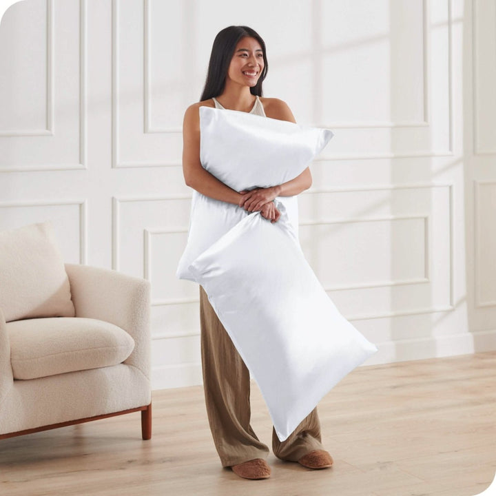 A woman standing while holding pillows with silk pillowcases on them