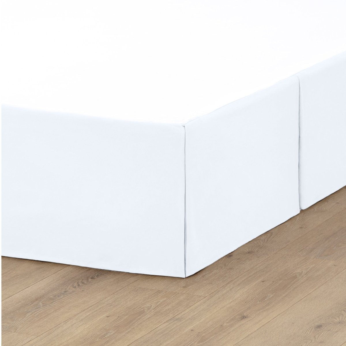 The corner of a box spring with a pleated bed skirt on it