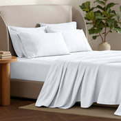 Bed sheets and pillows on a bed with a plant and side table in the background.