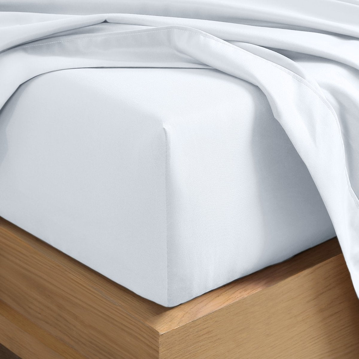 A close-up of a fitted sheet covering the corner of a bed frame, with matching top sheet draped over it.