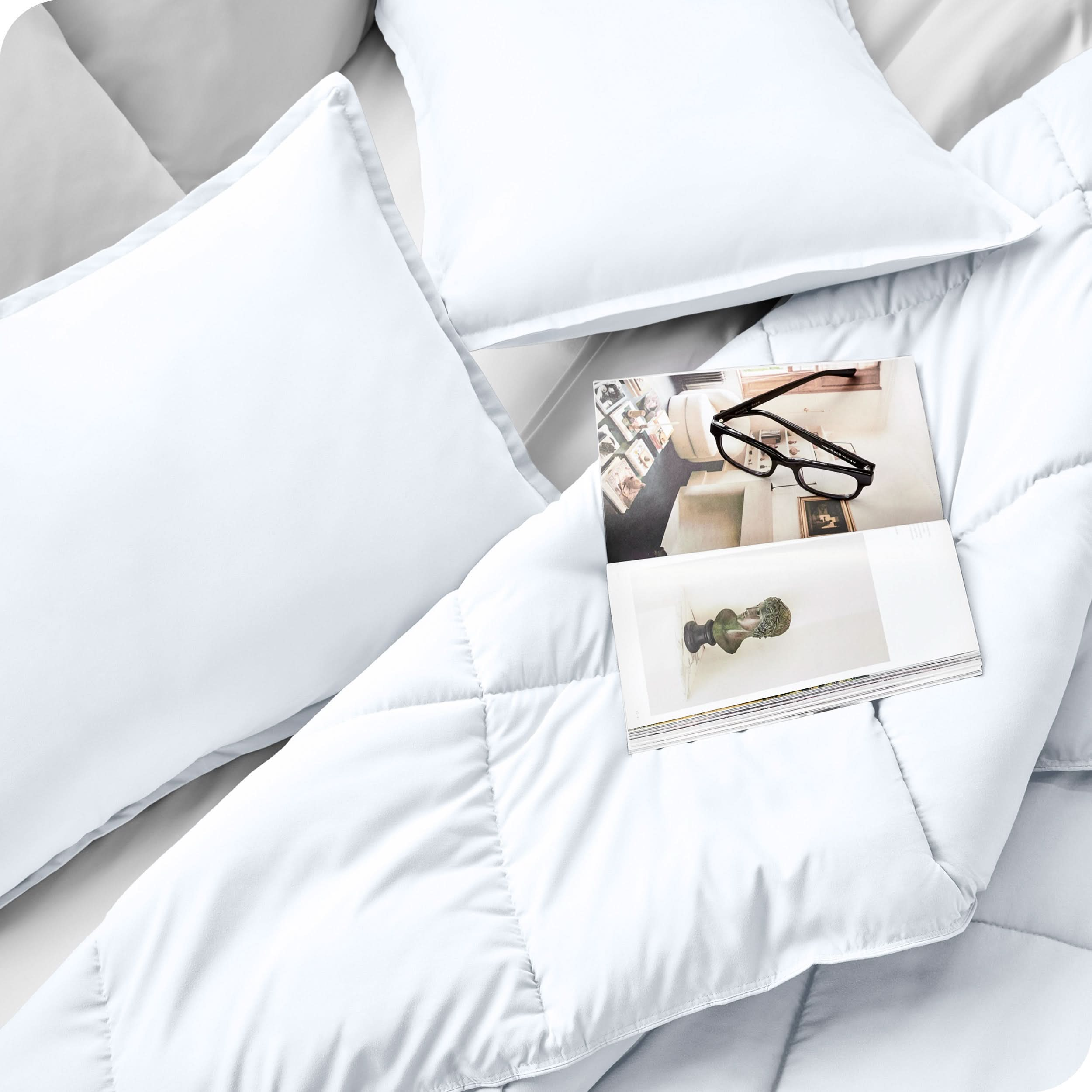 Close up of a comforter set on a bed. There are glasses and a magazine on top of the comforter.