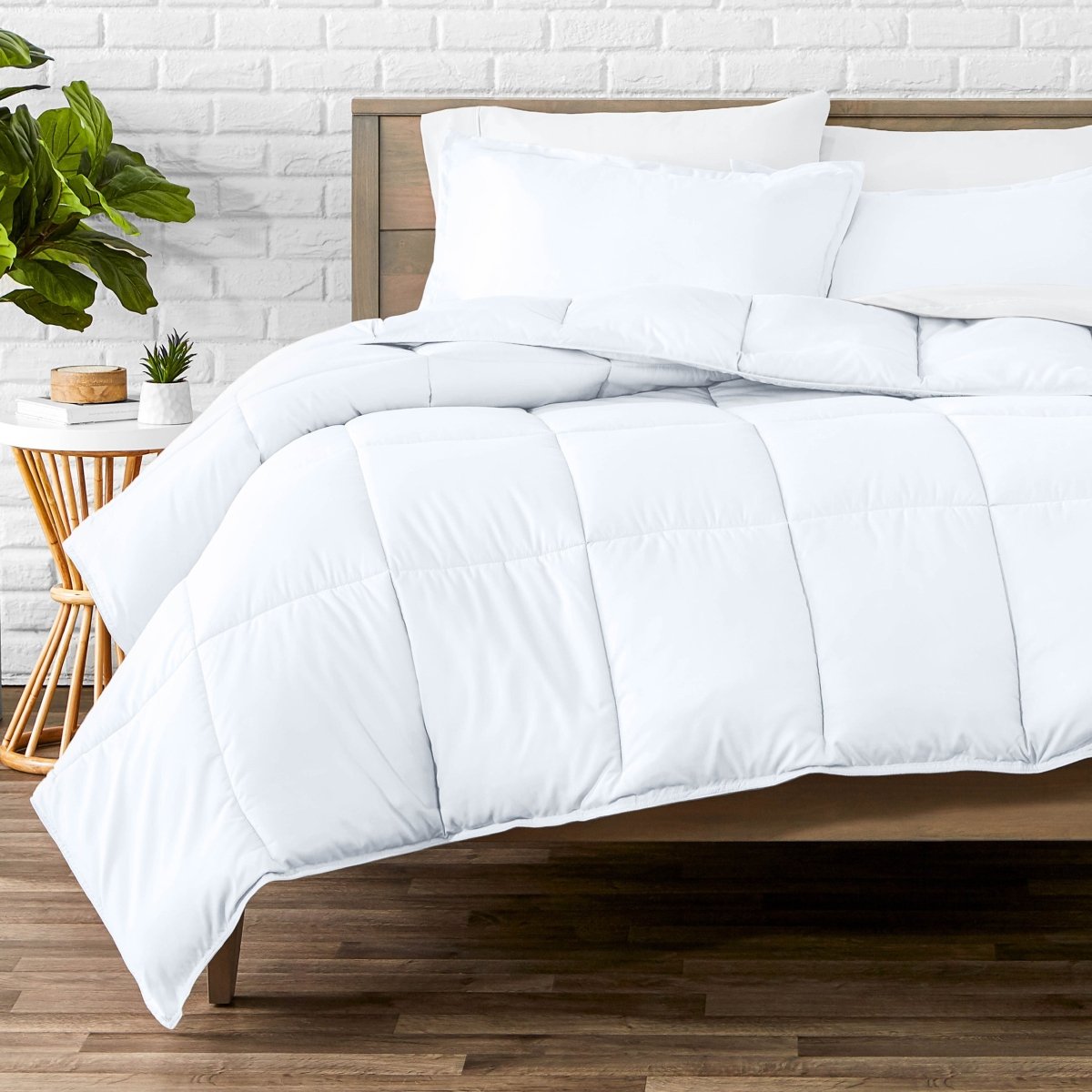 Comforter set on a bed with a white brick wall and plant in the background