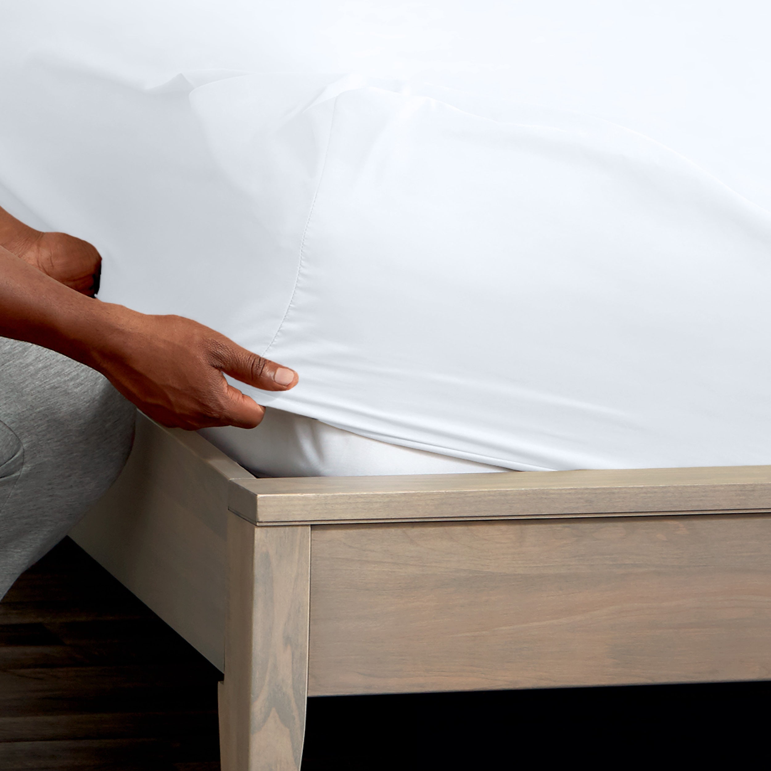 A man is putting a fitted sheet on a bed